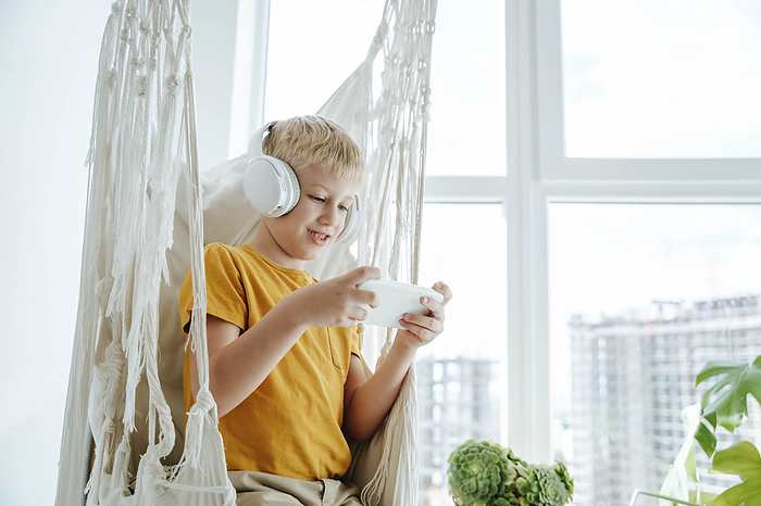 Boy wearing headphones in hammock and using mobile phone at home