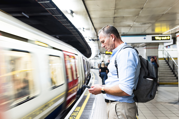 Businessman using smart phone and waiting for train on platform