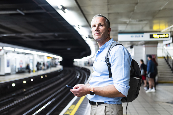 Businessman holding smart phone and waiting for train on platform