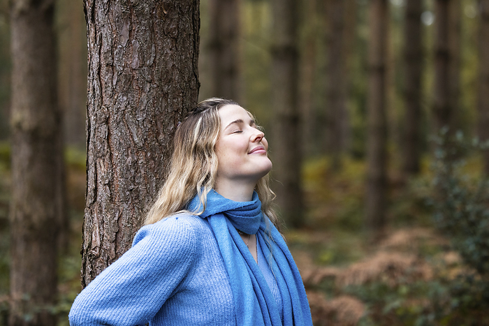 Smiling young woman standing with eyes closed near tree in forest