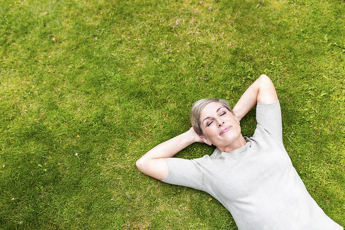 Carefree woman lying down with eyes closed on grass in garden