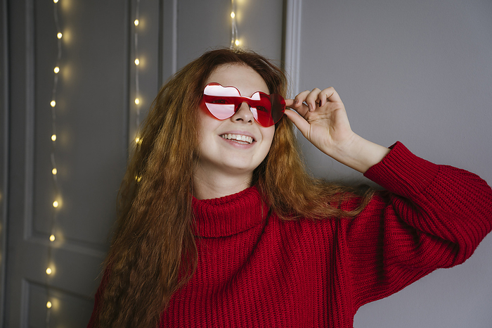 Smiling young woman wearing heart shaped sunglasses at home