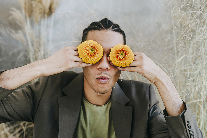 Businessman covering eyes with Gerbera daisies in garden