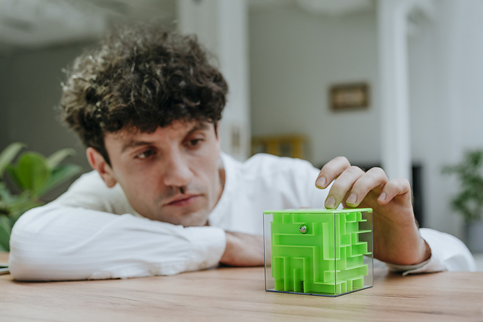 Thoughtful businessman with cube maze at desk in office