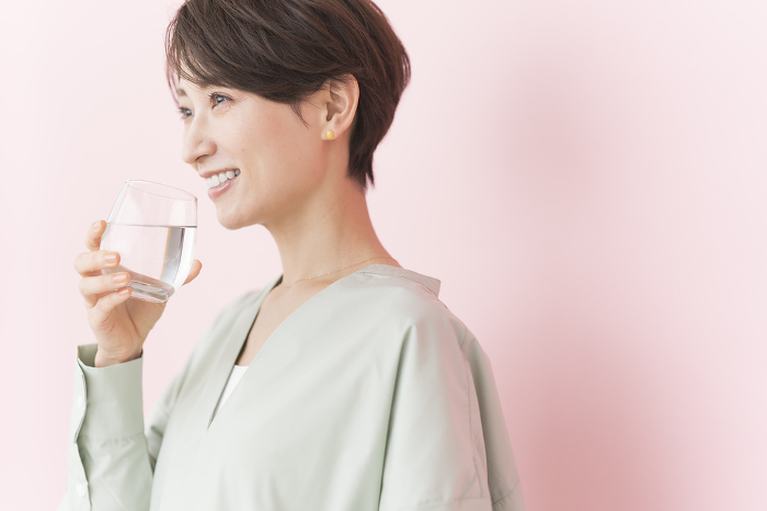 Japanese woman drinking clear drink/pink background (People)