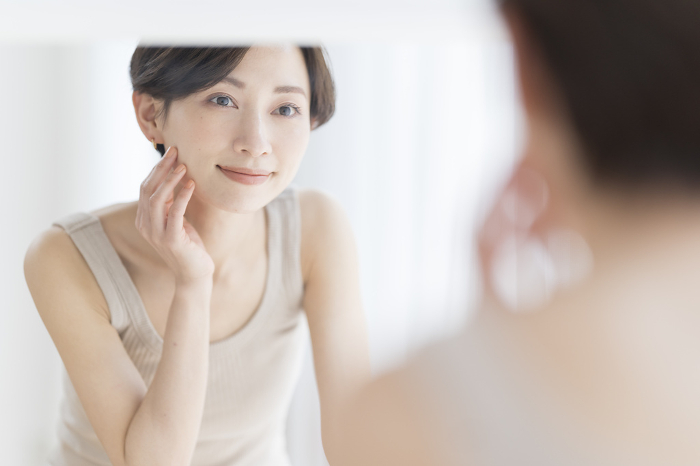 Beautiful Japanese woman doing skin care skin care while looking in the mirror in the morning (People)