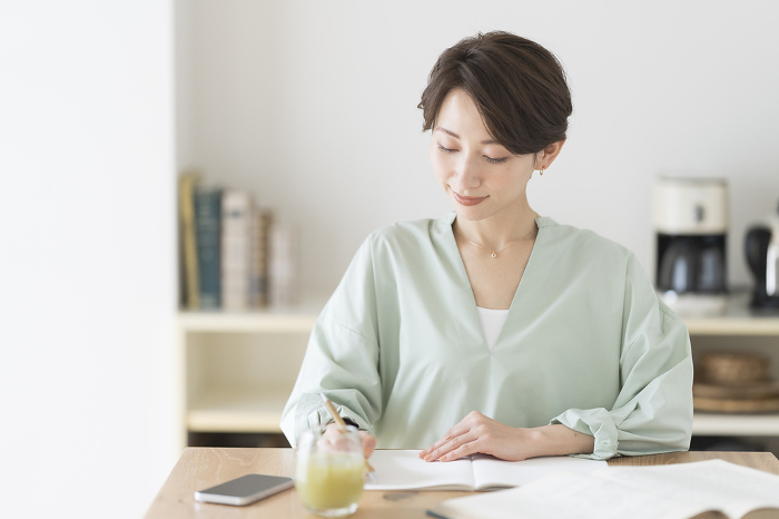 A middle-aged Japanese woman studying in a brightly lit room with natural light.