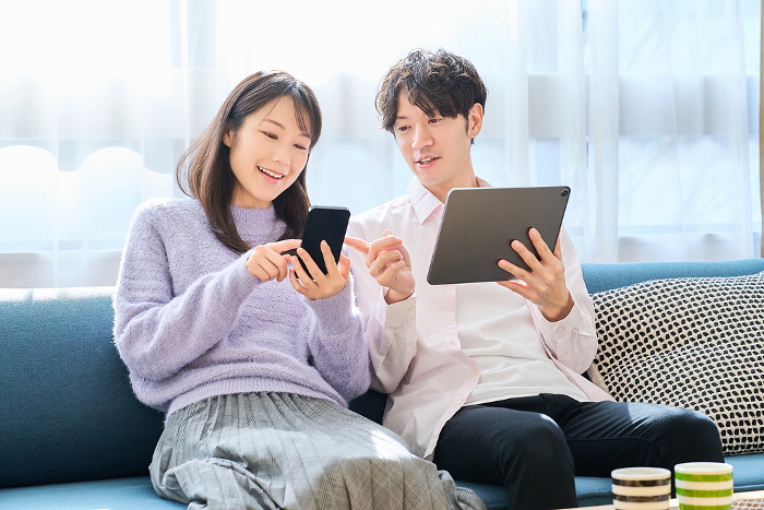 Japanese man and woman comparing smartphone and tablet PC screens (People)