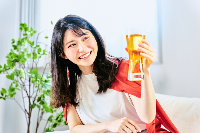A smiling Japanese woman in her 20s or 30s toasts with beer at a noon home party in her room on a holiday (People)