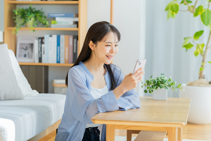Young Japanese woman looking at her phone while relaxing in her living room (People)