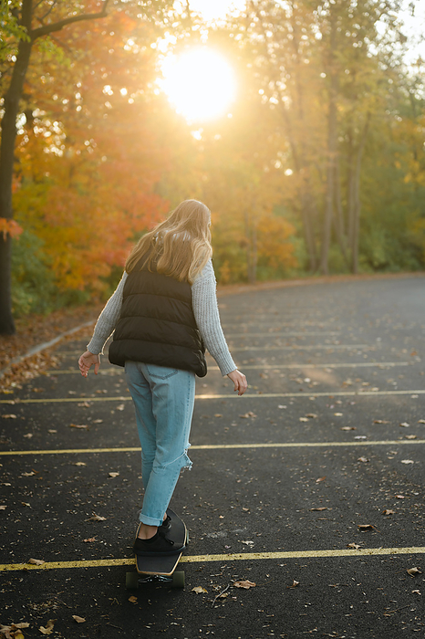 Rear view of woman longboarding in parking lot in the fall season, Chicago, Illinois, United States, by Cavan Images / Julia Maruyama