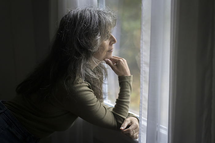 Older white woman in profile looks out of window, Harwich, Massachusetts, United States, by Cavan Images / Julia Cumes