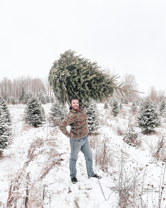 Man holding Christmas Tree Over Head Outside in Snow, Dushore, Pennsylvania, United States, by Cavan Images / Casey Kelly