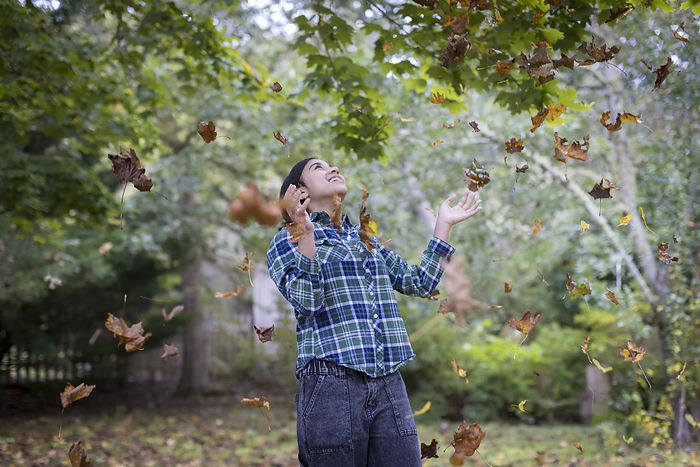 Biracial teen girl throwing up fall leaves and laughing, Harwich, Massachusetts, United States, by Cavan Images / Julia Cumes