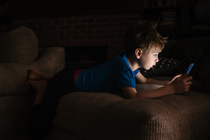 Young boy lays in dark room and looks at bright tablet, Reading, Pennsylvania, United States, by Cavan Images / Liz DeGroff