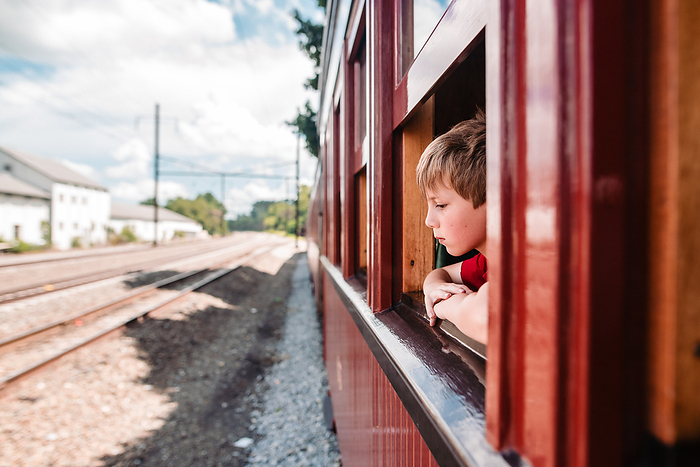 Side angle of boy looking out open train window at empty tracks, Reading, Pennsylvania, United States, by Cavan Images / Liz DeGroff