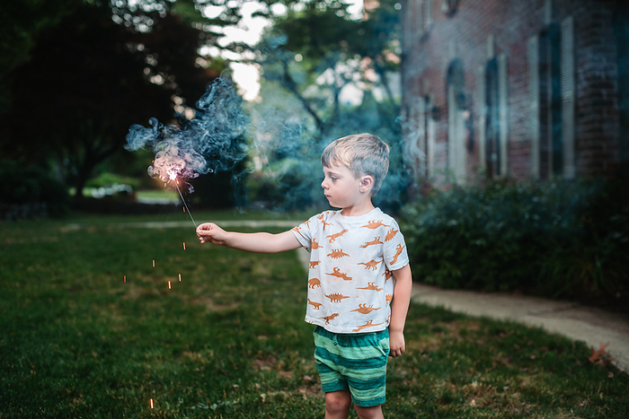 Preschooler holds and looks at sparkler while standing in front yard, Reading, Pennsylvania, United States, by Cavan Images / Liz DeGroff