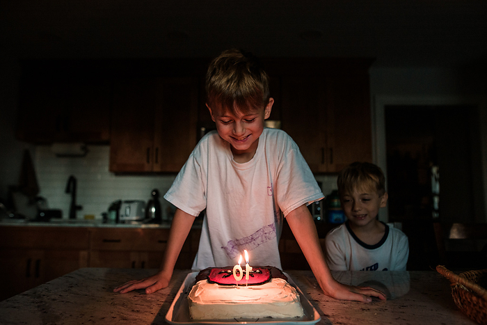 Young boy looks down at lit candles on birthday cake, Reading, Pennsylvania, United States, by Cavan Images / Liz DeGroff