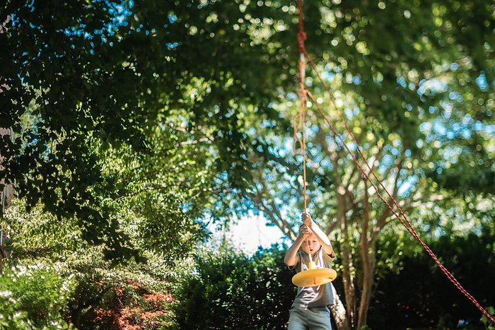 Wide shot of young boy preparing to jump on tree swing, Reading, Pennsylvania, United States, by Cavan Images / Liz DeGroff