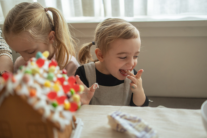 Girl giggles while decorating a gingerbread house with family, Vancouver, British Columbia, Canada, by Cavan Images / Sarah McKernan