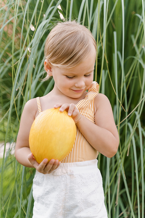 Little cute girl holding a yellow melon in her hands, Milan, Lombardy, Italy, by Cavan Images / Liza Zavialova