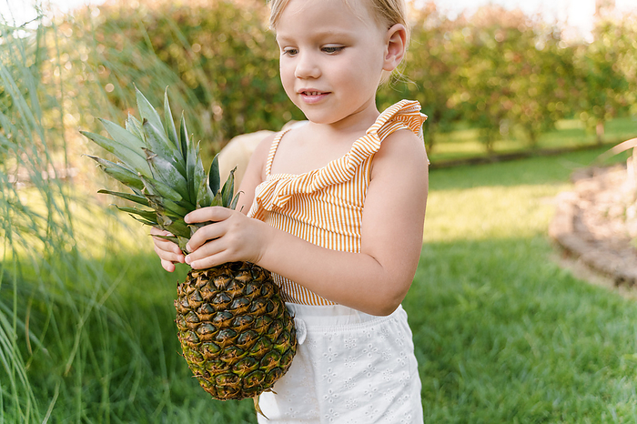 Little cute girl carries a pineapple in her hands, Milan, Lombardy, Italy, by Cavan Images / Liza Zavialova
