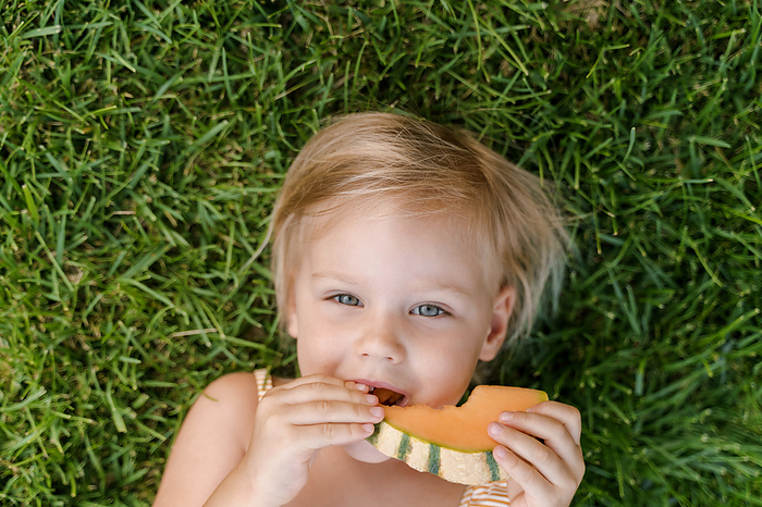 Time to eat fruit, cute girl eats melon while lying on the grass, Milan, Lombardy, Italy, by Cavan Images / Liza Zavialova