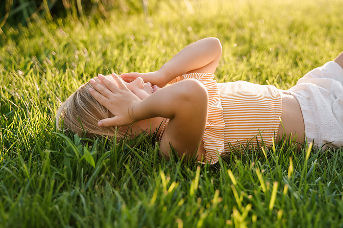 Baby girl lying on the grass and laughing, sunny weather, Milan, Lombardy, Italy, by Cavan Images / Liza Zavialova