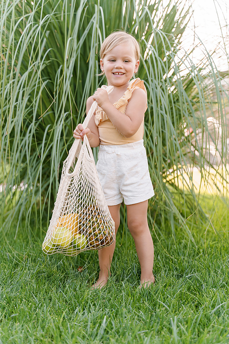 Little cute girl carries fruits in a string bag, Milan, Lombardy, Italy, by Cavan Images / Liza Zavialova