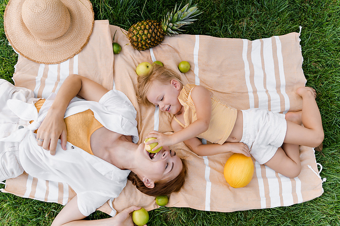 Mom and daughter are lying on a picnic, the girl feeds her mother, Milan, Lombardy, Italy, by Cavan Images / Liza Zavialova