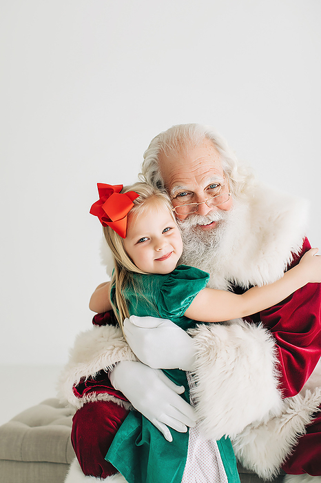 Toddler girl with a bow in her hair hugging santa claus, Atlanta, Georgia, United States, by Cavan Images / Jamie Sapp