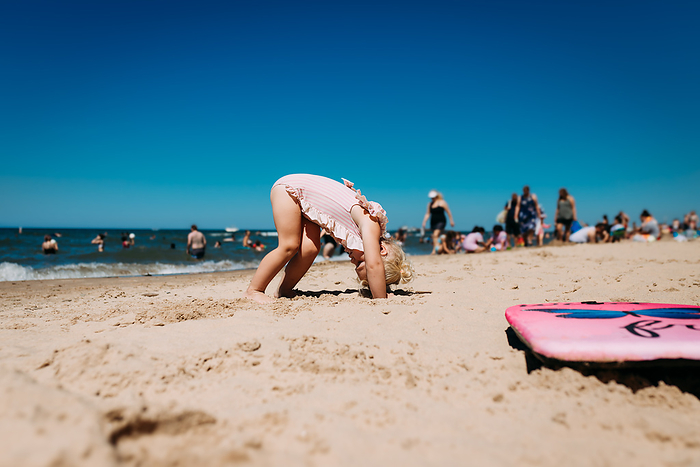 Young child doing downward dog yoga on crowded beach, Chesterton, Indiana, United States, by Cavan Images / Krista Taylor