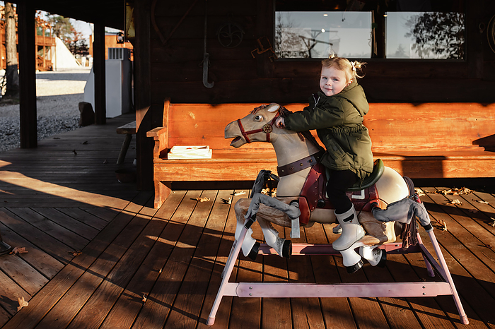 Child riding toy rocking horse on general store porch, Murfreesboro, Arkansas, United States, by Cavan Images / Krista Taylor