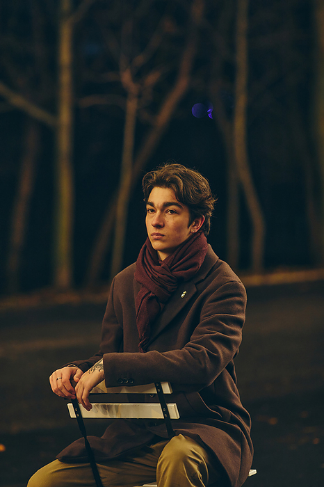 Portrait young man sitting on the chair outdoors in the city at night, Chișinău, Chisinau, Moldova, by Cavan Images / Elena Perevalova