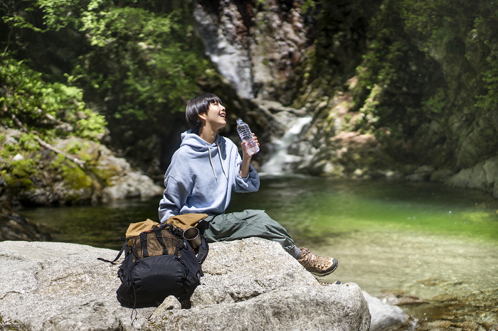 Young Japanese woman trekking / sitting on a rock in the canyon drinking water (People)