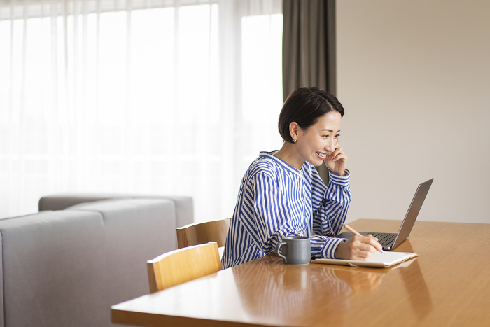 Middle Japanese woman taking notes on her laptop at home.