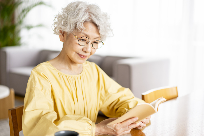 Senior Japanese woman reading a book wearing reading glasses (People)