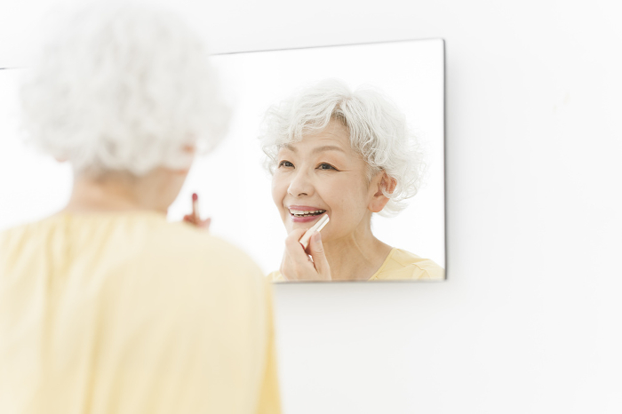 Senior Japanese woman applying lipstick in front of a mirror (People)
