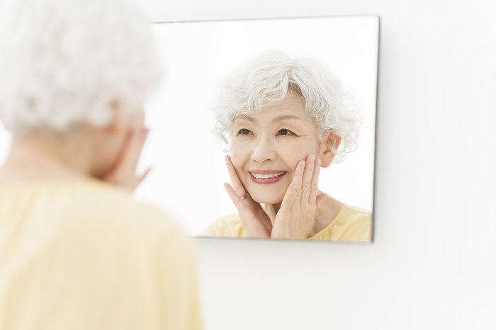Japanese senior woman taking care of her skin in the mirror (People)