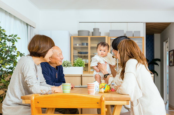A Japanese family of five: a baby standing on a desk, a father and mother assisting him, and a grandmother and grandfather watching over him (People)