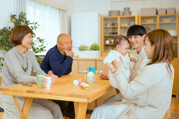 A Japanese family of five: a mother sitting in her living room holding her baby, a father watching over her, a grandfather, and a grandmother (People)