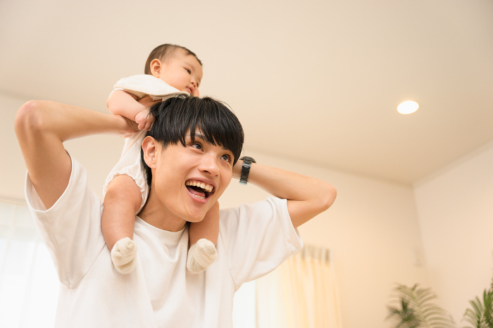 A smiling father of a man in his 20s or 30s entertaining his 0-year-old baby on his shoulders (Japanese / People)