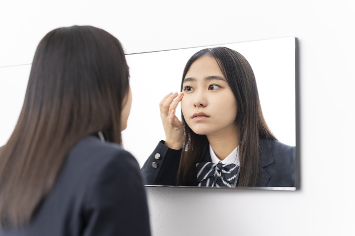 Japanese high school girl looking in mirror / trying to put on contact lenses.
