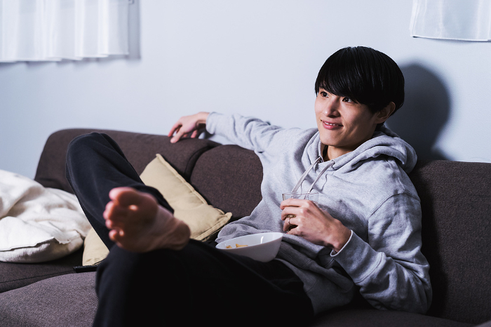 Young Japanese man relaxing at home, watching TV and videos to relieve stress (People)