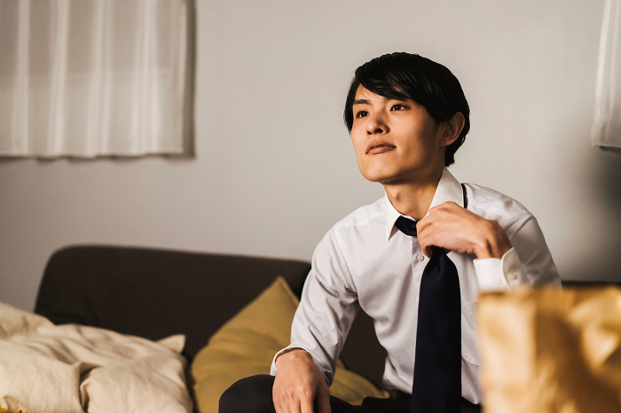 A Japanese man in his 30s, exhausted from working overtime, comes home and sits on his couch watching TV.