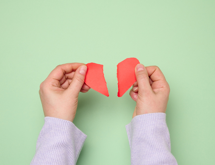 Two female hands tearing a red paper heart, symbolizing divorce or disappointment in relationships Two female hands tearing a red paper heart, symbolizing divorce or disappointment in relationships