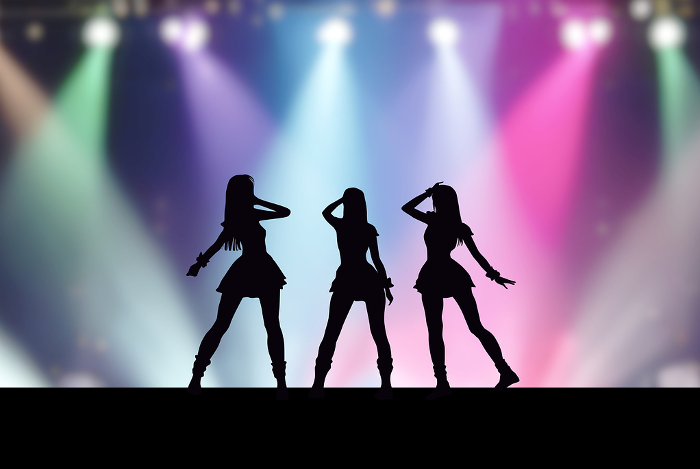 Three female idols on stage with colorful spotlights
