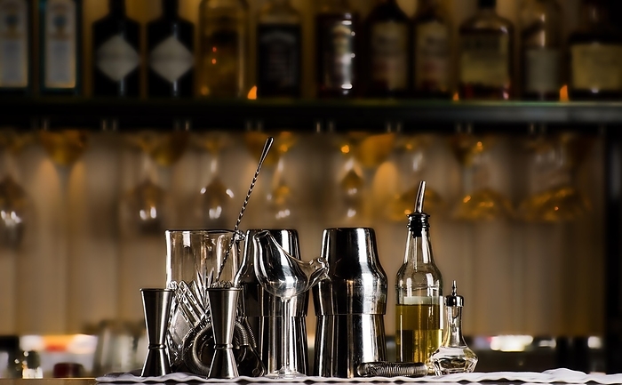 Set of bar accessories for making cocktails, located on the bar, behind is a shelving with liqueurs and strong alcohol., by Andrei Zaretski