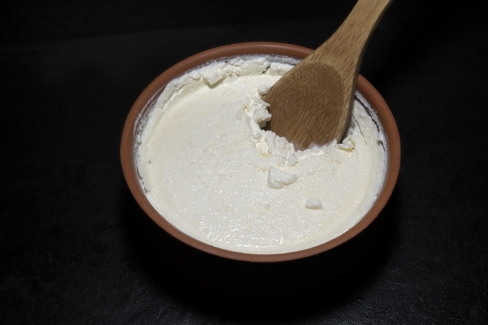 Original Turkish Kaymakli yoghurt matured in a clay bowl, with a wooden spoon, food photography with black background, by Siegra Asmoel