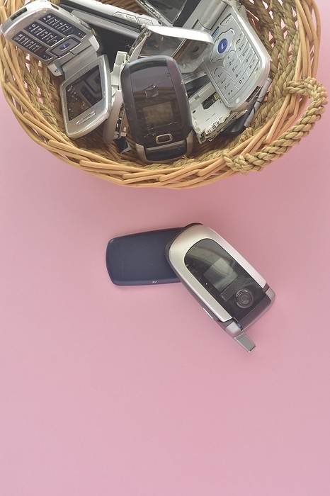 An assortment of vintage mobile phones in a basket with one flip phone placed in front, poker cards and chips, by carlos l vives